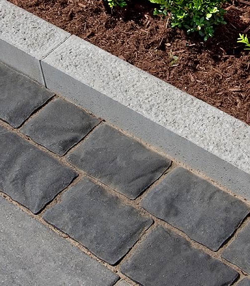 Light grey concrete curb separating mulched garden bed and pacving stone driveway